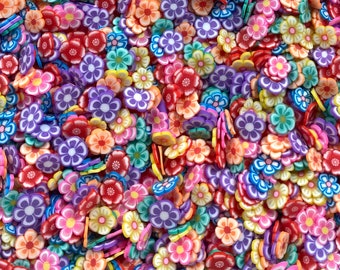 Op de afbeelding: Een close-up afbeelding van een grote verzameling kleurrijke bloemvormige polymer clay-bedels. De bedels zijn in verschillende tinten roze, paars, blauw, groen, geel en rood.