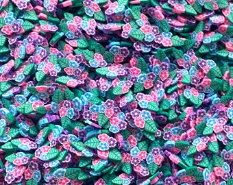 Op de afbeelding: Een grote verzameling kleurrijke polymer clay bloem- en blaadjescharms. De charms zijn in tinten roze, paars, blauw en groen.