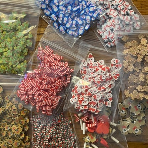 May include: Assortment of Christmas-themed polymer clay sprinkles in various colors and shapes, including candy canes, Santa hats, gingerbread men, and Christmas trees. The sprinkles are packaged in clear plastic bags.