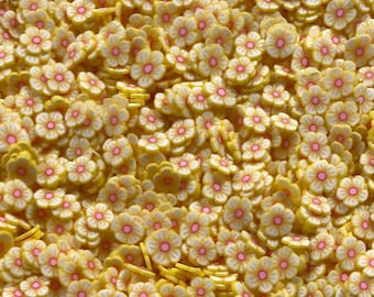 Op de afbeelding: Een grote hoeveelheid gele, bloemvormige polymer clay sprinkles met roze centra.