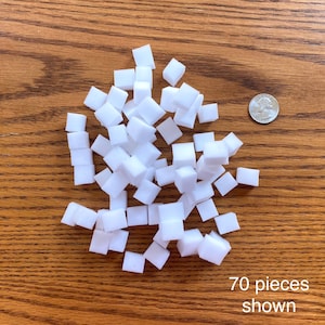 May include: A pile of 70 white foam cubes on a wooden surface. 70 pieces shown.