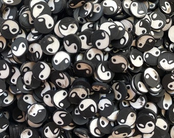 May include: A close-up image of a large quantity of black and white yin yang symbol charms. The charms are small and round, and they are scattered randomly across the surface.