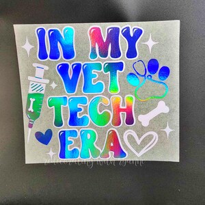 May include: A holographic vinyl sticker with the text "In My Vet Tech Era" in rainbow colors. The sticker includes a paw print, a bone, a heart, and a syringe.