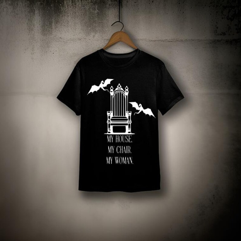 May include: Black t-shirt with a white graphic of a throne with two bats flying above it. The text "MY HOUSE. MY CHAIR. MY WOMAN." is printed below the throne.