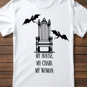 May include: White t-shirt with a black graphic of a throne with two dragons flying above it. The text below the throne reads "My House. My Chair. My Woman."
