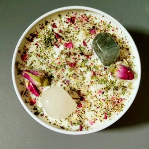 May include: White candle with green herbs, rose petals, and clear and green crystals.