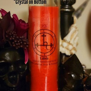 May include: An 18 ounce red glass candle jar with a black and white sigil and the text "Lilith" and "Apple & Sandalwood Scent with Carnelian, Rose & Patchouli". The jar is labeled "7 Day Jar" and "*Crystal on Bottom".