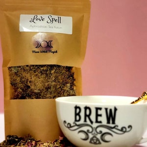 May include: A brown paper pouch with a label that reads "Love Spell Aphrodisiac Tea Potion" and a moon and stars symbol. The pouch is filled with dried herbs and is sitting next to a white mug with the word "BREW" written on it.
