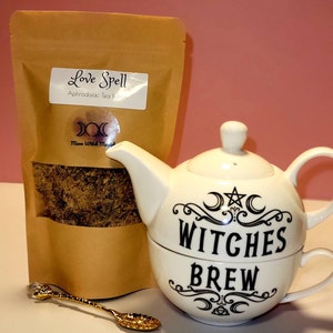May include: A brown paper bag with the text "Love Spell Aphrodisiac Tea Potion" and a white teapot with the text "Witches Brew" and a crescent moon and star design. A gold spoon is in the foreground.