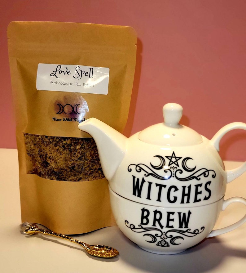 May include: A brown paper bag with the text "Love Spell Aphrodisiac Tea Potion" and a white teapot with the text "Witches Brew" and a crescent moon and star design. A gold spoon is in the foreground.