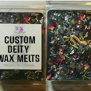 May include: Two wax melts in clear plastic packaging. The wax melt on the left has a white label with the text "CUSTOM DEITY WAX MELTS". The wax melt on the right is black with gold, red, and green accents.