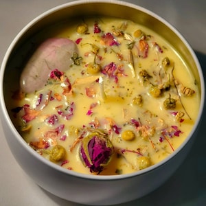 May include: A yellow candle with dried flowers and herbs, including rose petals, chamomile, and lavender, in a white ceramic container.