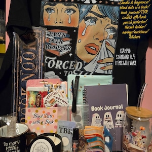 May include: A collection of book-themed items, including a black t-shirt with a crying woman graphic and the text "BORN TO READ." Other items include a mug, candle, journal, stickers, and a tumbler.