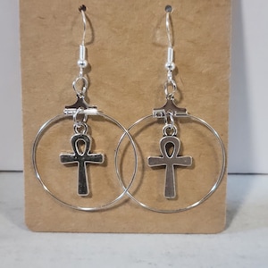 May include: Silver hoop earrings with a silver ankh pendant hanging from each hoop.
