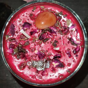 May include: A red candle with dried rose petals, herbs, and a carnelian crystal. The candle is in a clear glass jar.