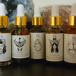 Puede incluir: Cinco pequeños frascos de vidrio con tapas y etiquetas doradas. Cada frasco contiene una mezcla de aceite diferente para el trabajo de la deidad, las invocaciones y las ofrendas. Las etiquetas presentan ilustraciones de deidades, incluyendo Loki, Isis, Perséfone, Hécate y Lilith.