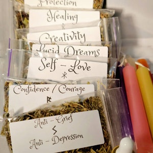 May include: A set of eight small bags of dried herbs with labels for various intentions, including protection, healing, creativity, lucid dreams, self-love, confidence, anti-grief, and anti-depression. Three candles and a small bottle of oil are also included.