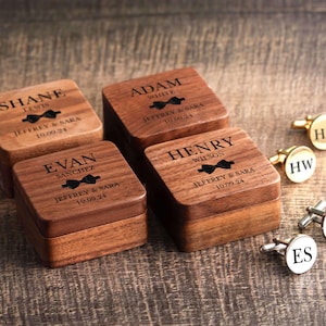 May include: Four wooden boxes with engraved names, dates, and bowties. Each box has a different name and date. The boxes are arranged in a row. There are also four pairs of cufflinks with initials on them.