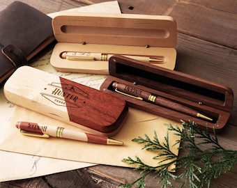 May include: Three wooden pens with gold-tone accents and matching wooden cases. One pen is light wood, one is dark wood with the name VINCENT, and one is two-toned with the name HUNTER and the text TEXAS engraved on the case and pen body.