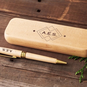 Op de afbeelding: Een houten pen en een houten doos met een geometrisch ontwerp en de gegraveerde initialen "A.E.S.".