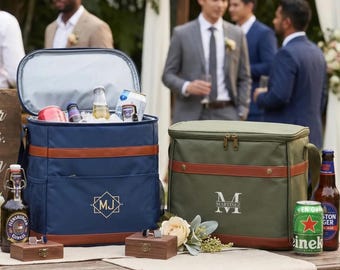 May include: Two rectangular insulated cooler bags, one navy blue and one olive green, each featuring brown faux leather trim and a personalised monogram. The navy bag displays 'MJ' in a geometric frame, while the olive bag shows 'MARTINEZ'.