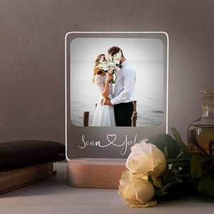 May include: A white LED light up photo frame with a picture of a couple kissing. The frame has a wooden base and the text "Scan & Juli" is written on the front.