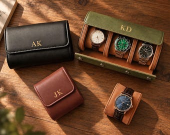 May include: A black watch roll with the initials AK, a brown watch case with the initials JK, and an olive green watch box with the initials KD containing three wristwatches. A separate wristwatch with a dark blue face rests on a tan cushion.