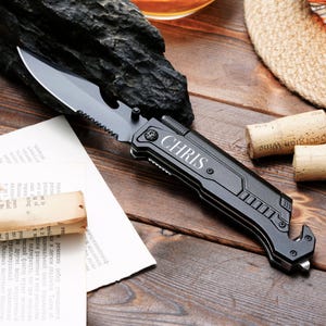 May include: Black multi-tool pocket knife with a serrated blade, bottle opener, and a safety belt cutter. The knife has a black handle with a silver engraved name "CHRIS".