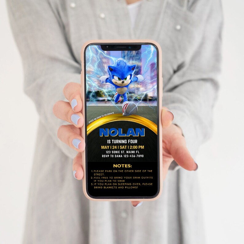 May include: A smartphone displays a birthday party invitation featuring Sonic the Hedgehog. The invitation includes the name "Nolan", date, time, and address. Additional notes are listed below the details. The phone is held by a person.