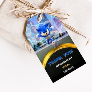 May include: A gift tag featuring Sonic the Hedgehog with a blue and white color scheme, lightning bolts, and the text "THANK YOU!" in blue. The tag is attached to a wrapped gift with a raffia bow.