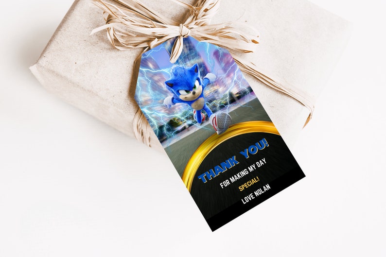 May include: A gift tag featuring Sonic the Hedgehog with a blue and white color scheme, lightning bolts, and the text "THANK YOU!" in blue. The tag is attached to a wrapped gift with a raffia bow.