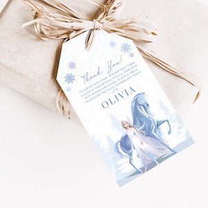 May include: A white thank you tag with a blue and white snowflake design. The tag features a cartoon image of a girl with long blonde hair wearing a blue dress and riding a white horse. The text on the tag reads "Thank You! To guests who came with birthday cheer in gowns and crowns, you all were dear with wishes and songs in joyful array. Thanks for the magic you brought today. Love, Olivia."