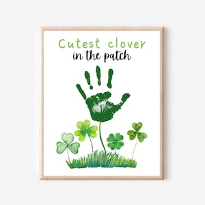 May include: A green handprint with the text "Cutest clover in the patch" above it. The handprint is surrounded by green shamrocks and green grass.