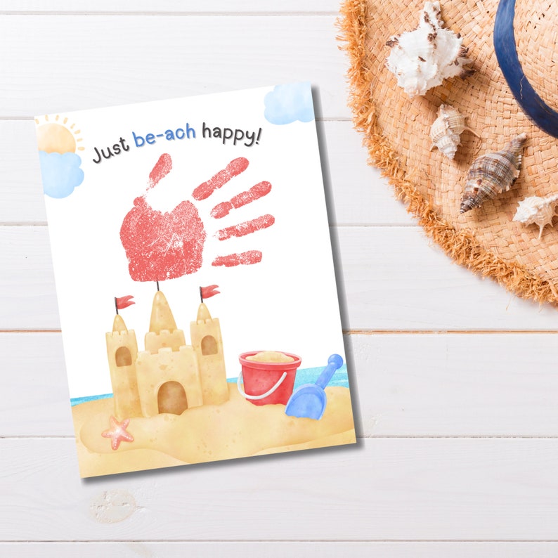 K&ouml;nnte beinhalten: Eine wei&szlig;e Karte mit einem roten Handabdruck und dem Text "Just be-ach happy!" Ein gelbes Sandburg mit blauen Flaggen, einem roten Eimer und einer blauen Schaufel befinden sich am Strand.