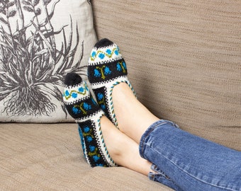 May include: A pair of blue and white knitted slippers with a geometric pattern. The slippers are worn by a person sitting on a couch with their legs crossed.