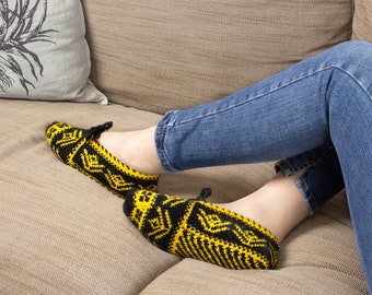 May include: A person wearing blue jeans and yellow and black knitted slippers is relaxing on a couch.