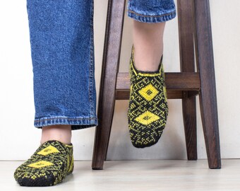 May include: A pair of black and yellow patterned socks with a diamond design. The socks are worn on a person's feet.
