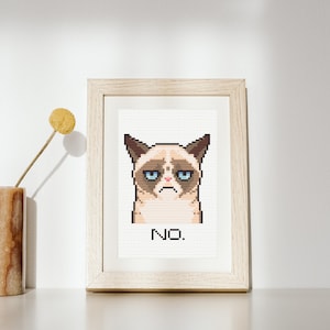 May include: A framed cross-stitch featuring a pixelated image of a grumpy cat with the word "NO." underneath.