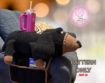 May include: A black and brown crochet dachshund armrest organizer with pockets, holding a pink tumbler with a straw. The organizer is on a gray couch arm. Text on the image reads "PATTERN ONLY NOT AI" and "www.PearlsWithCarey.com".