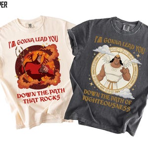 May include: Two t-shirts, one ivory and one pepper, with graphic designs. The ivory shirt features a red devil illustration with the text "I'M GONNA LEAD YOU DOWN THE PATH THAT ROCKS." The pepper shirt has an angel illustration and the text "I'M GONNA LEAD YOU DOWN THE PATH OF RIGHTEOUSNESS."