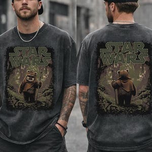 May include: A charcoal grey, acid-washed short-sleeve t-shirt featuring a graphic print of an Ewok from Star Wars standing in a forest. The Star Wars logo is printed in a muted green color above the character. The design appears on the front.