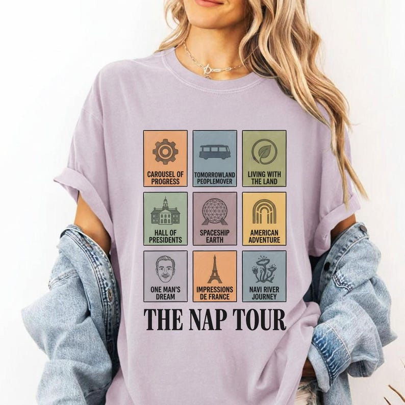 May include: A light purple t-shirt with a graphic featuring nine colorful squares, each with an image and text. The text reads "CAROUSEL OF PROGRESS", "TOMORROWLAND PEOPLEMOVER", "LIVING WITH THE LAND", "HALL OF PRESIDENTS", "SPACESHIP EARTH", "AMERICAN ADVENTURE", "ONE MAN'S DREAM", "IMPRESSIONS DE FRANCE", and "NAVI RIVER JOURNEY". The text "THE NAP TOUR" is below the squares.