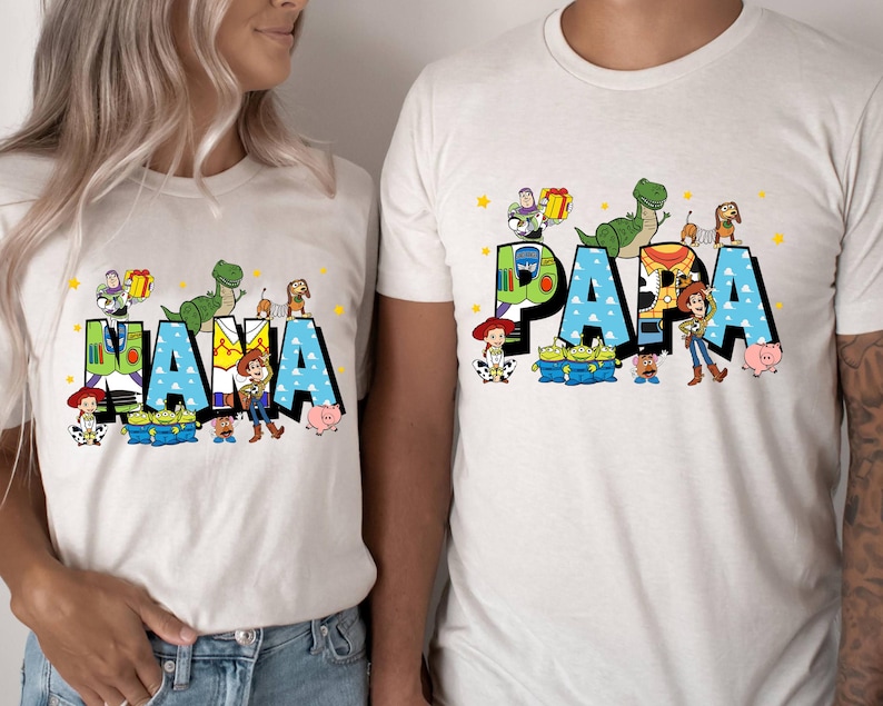 K&ouml;nnte beinhalten: Wei&szlig;e T-Shirts mit den W&ouml;rtern "MAMA" und "PAPA" in gro&szlig;en, farbenfrohen Buchstaben. Die Buchstaben sind mit Zeichentrickfiguren verziert. Die Shirts sind ein passendes Set, perfekt f&uuml;r eine Familie.