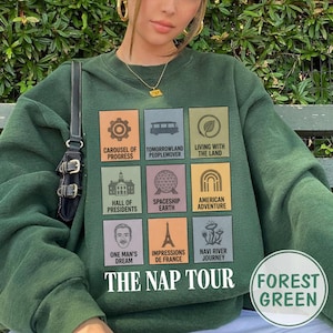 May include: Forest green sweatshirt with a graphic featuring nine colorful squares with theme park icons and text. The text includes "Carousel of Progress," "Tomorrowland Peoplemover," and "The Nap Tour." The sweatshirt also has the words "Forest Green."