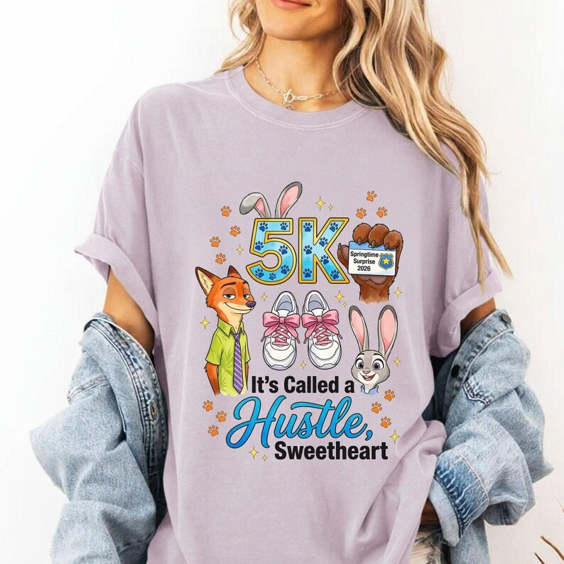 May include: A lilac t-shirt with a colourful graphic. The design includes cartoon characters, running shoes, and the text "5K It's Called a Hustle, Sweetheart". The design also includes paw prints and the words "Springtime Surprise 2020".