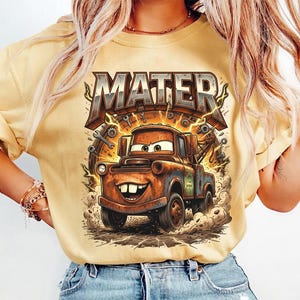 May include: Yellow t-shirt featuring a cartoon image of Mater from the movie Cars. The graphic includes the word "MATER" in a bold, textured font above the character. The design is detailed with lightning bolts and mechanical elements.