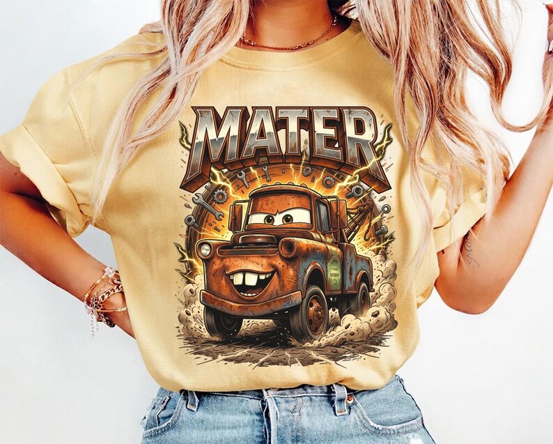 May include: Yellow t-shirt featuring a cartoon image of Mater from the movie Cars. The graphic includes the word "MATER" in a bold, textured font above the character. The design is detailed with lightning bolts and mechanical elements.