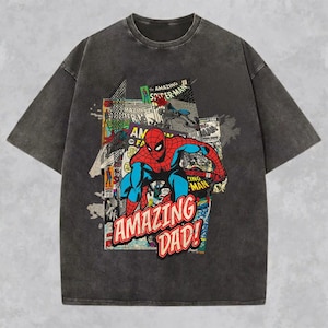 May include: Dark gray t-shirt featuring a comic book style graphic of Spider-Man in red and blue, with the text "AMAZING DAD!". The shirt has a vintage, washed look.