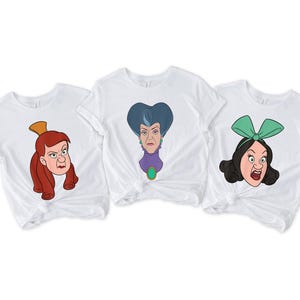 May include: Three white t-shirts featuring cartoon illustrations of female characters with angry expressions. The characters have red, blue, and black hair, and are wearing accessories like a gold crown and a green bow.