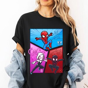 May include: Black t-shirt featuring a colorful comic-style graphic of Spider-Man and other Spider-Verse characters. The design includes a blue, red, and pink color scheme with cartoon illustrations of the superheroes.
